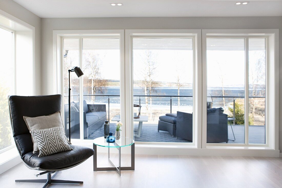 Schwarzer Leder Lounge Sessel mit Kissen und Beistelltisch vor Terrassentüren, Blick auf See