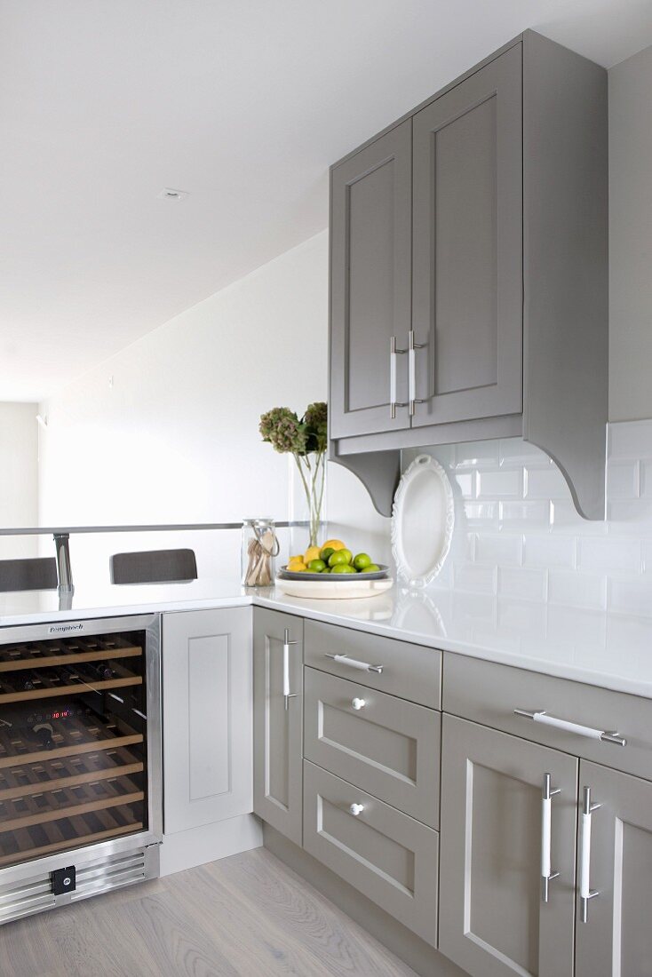 Corner of kitchen with white worksurface on grey-painted base units and wine chiller