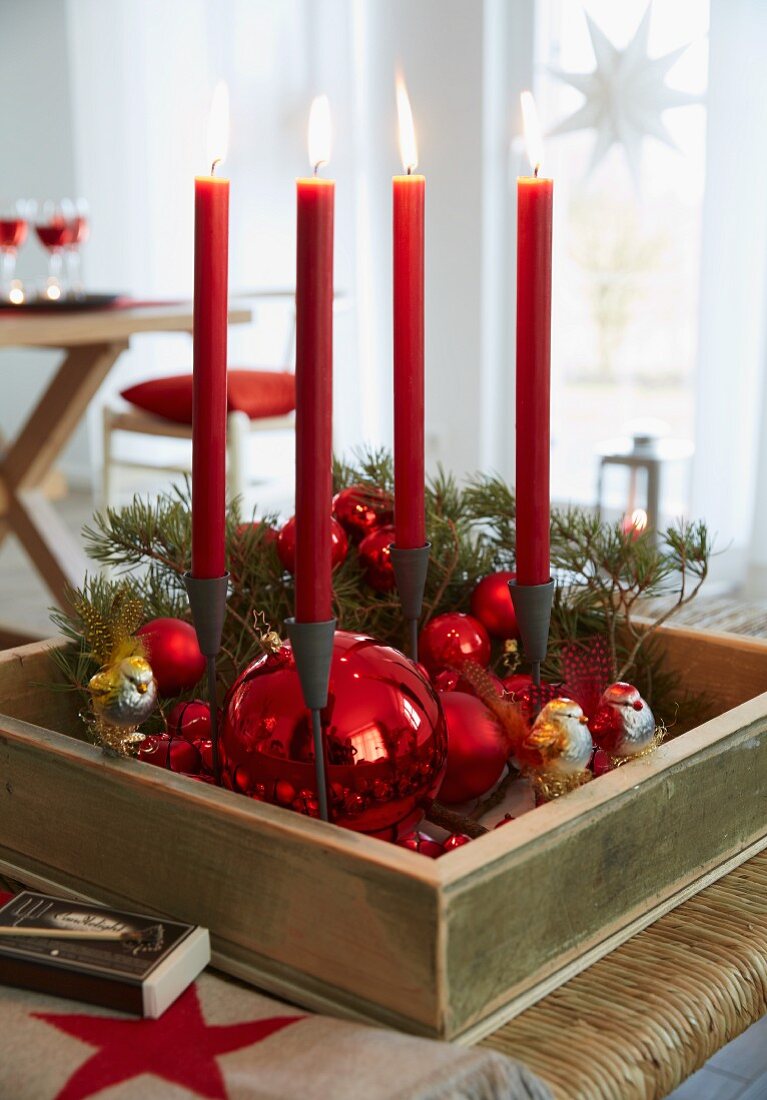 Adventskranz in Holzkasten mit roten Weihnachtskugeln und vier roten, brennenden Kerzen