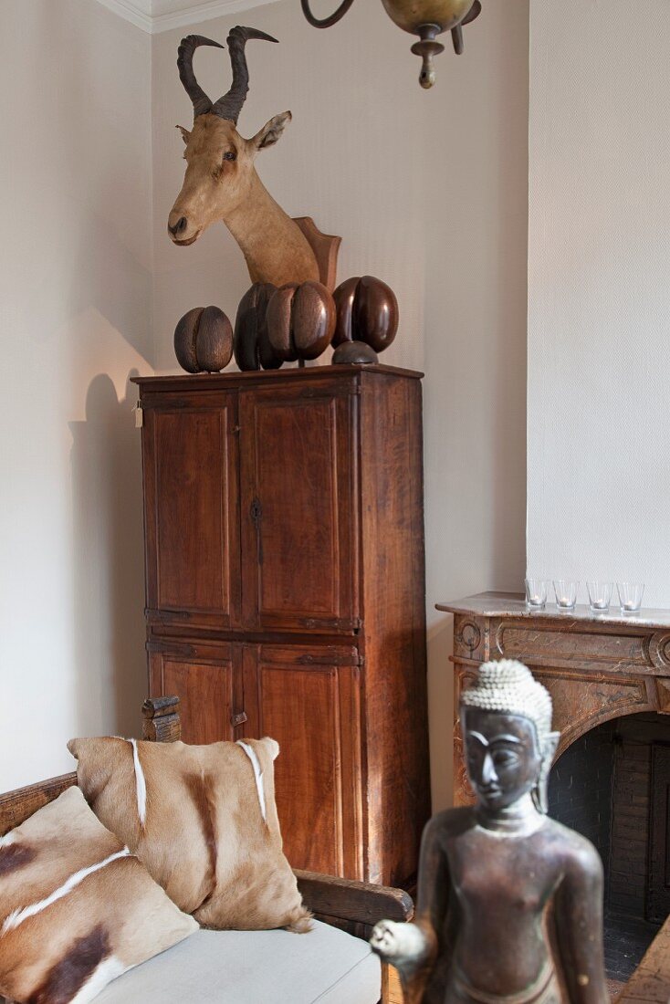 Hunting trophy above antique cupboard, Oriental sculpture and couch with animal-skin cushions