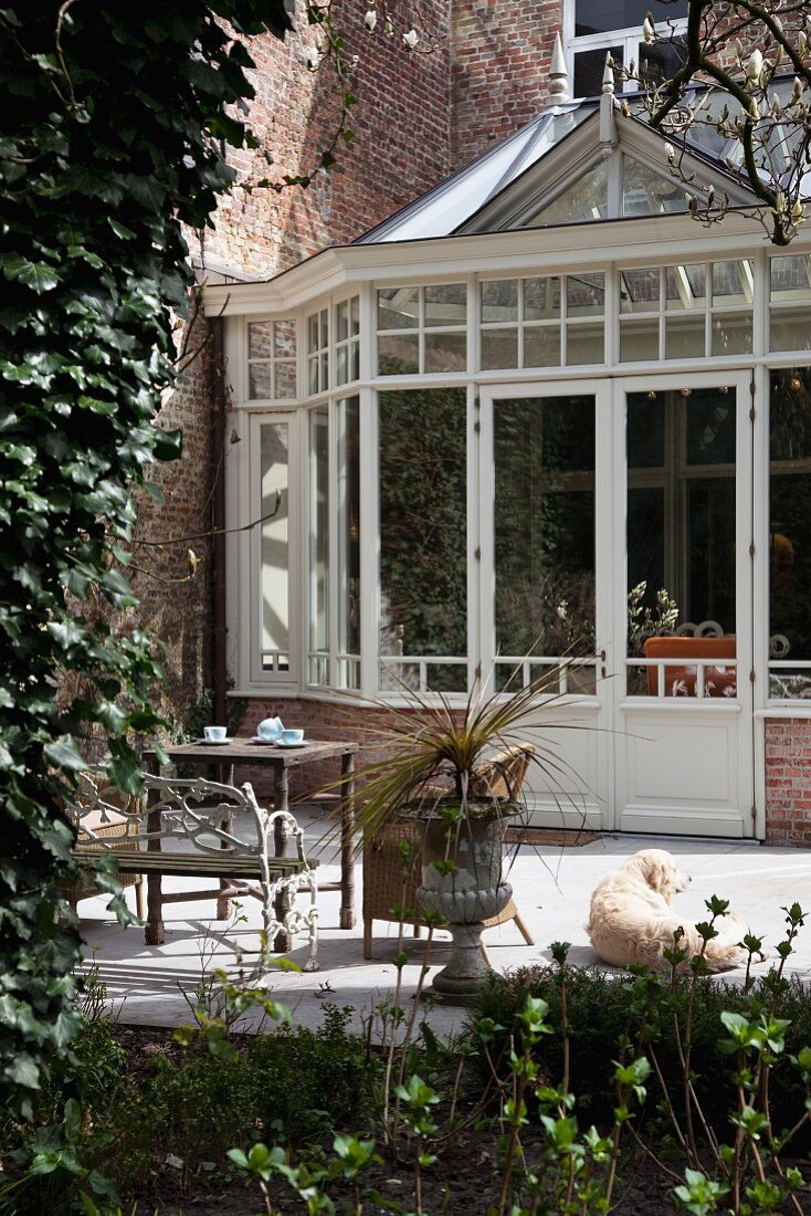 Traditional conservatory adjoining manor house and antique garden furniture on sunny terrace