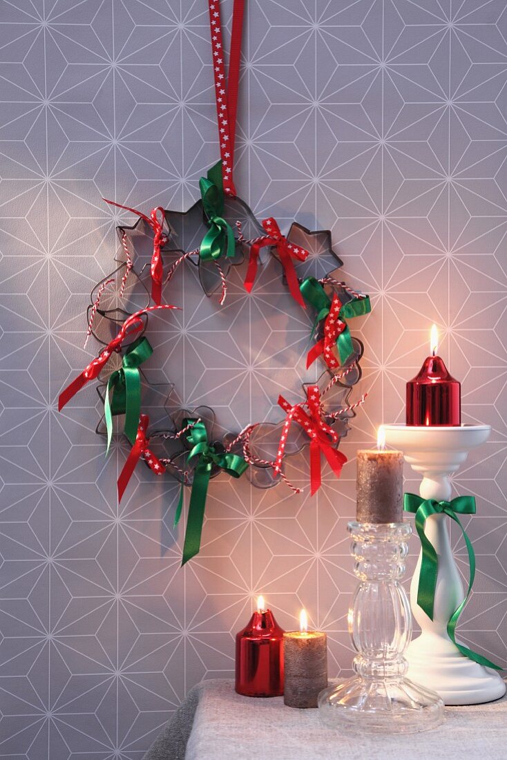 Festive wreath of pastry cutters and ribbons on wall above candlesticks