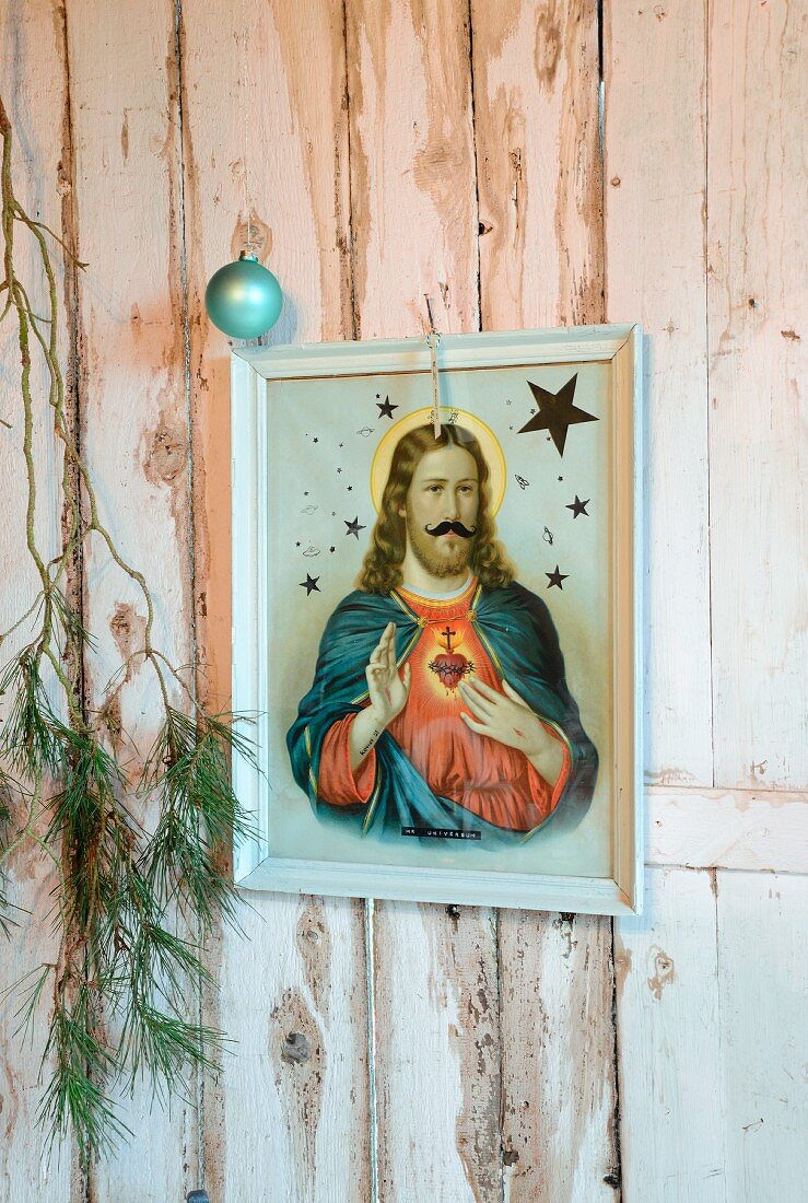 Gerahmtes Heiligenbild mit Föhrenzweig und Weihnachtskugel auf weißer, rustikaler Holzwand