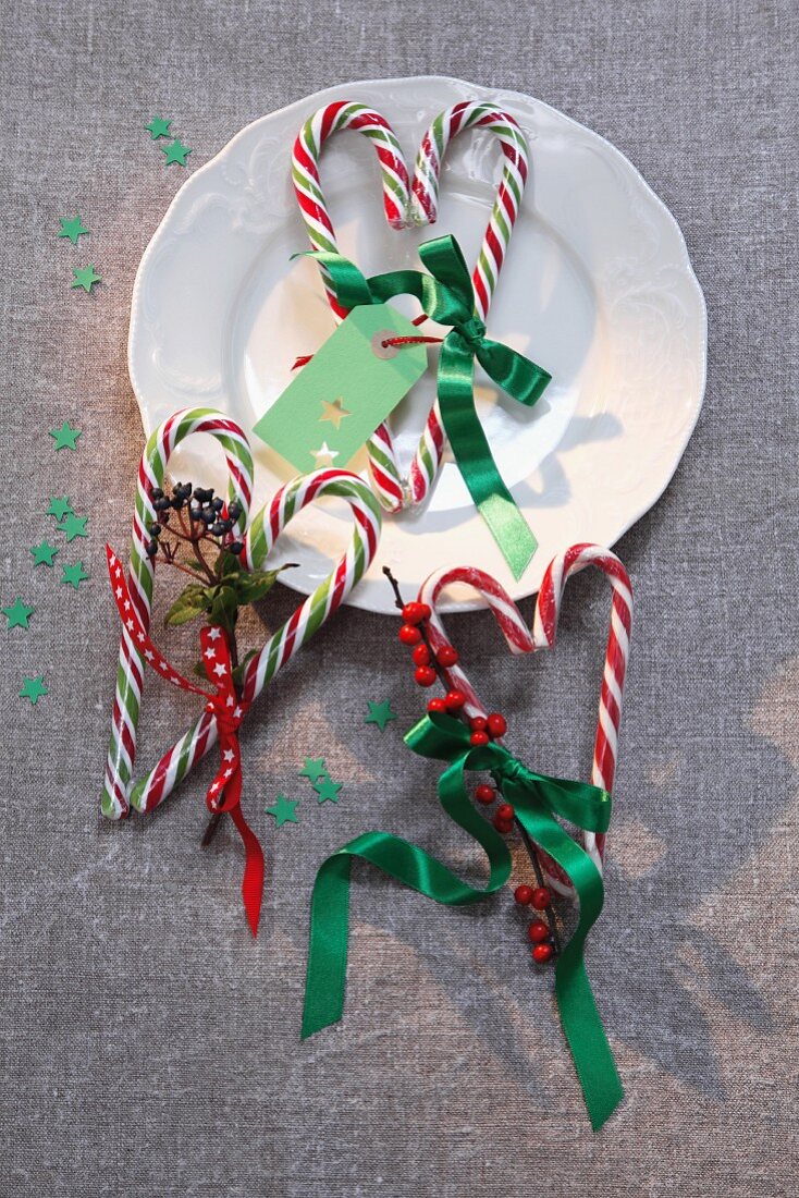 Zuckerstangen zu Herzform zusammengelegt, verziert mit Schleifenband und Beerenzweigen als weihnachtliche Tischdeko