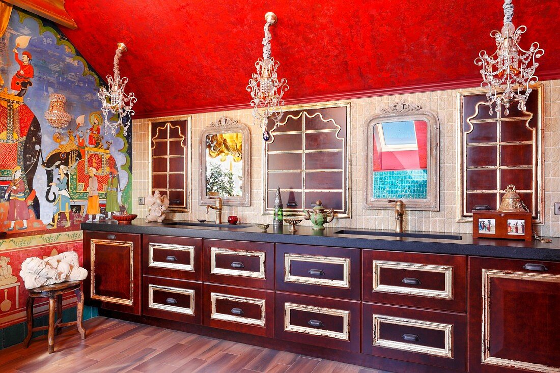 Orientalisch gestaltete Küche - Holzunterschränke mit vergoldeten Profilen in langer Küchenzeile, unter filigranen Kronleuchtern an roter Decke