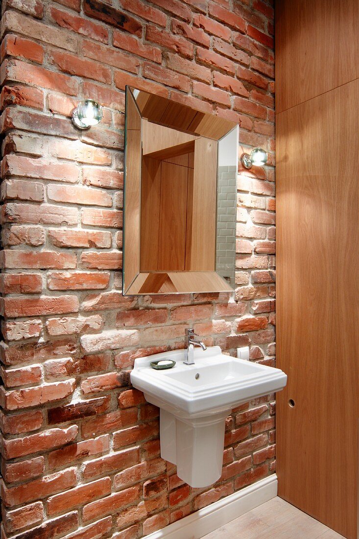 Vintage sink and mirror on rustic brick wall with modern wooden cabinet to one side