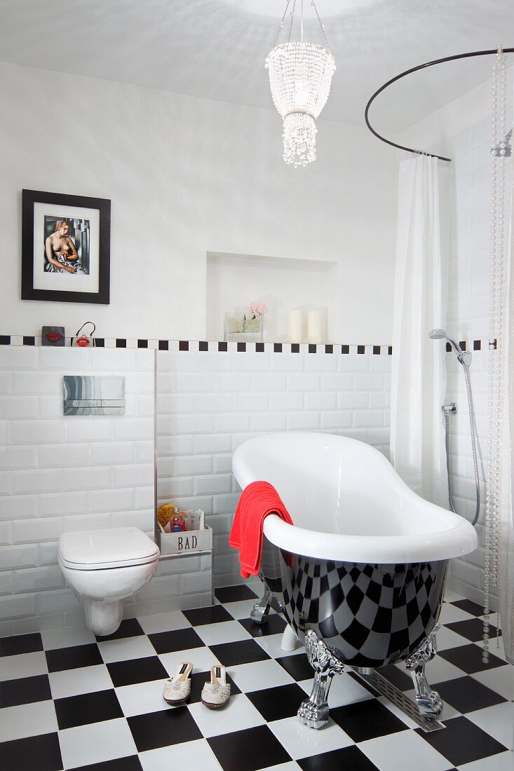 Free-standing, vintage bathtub on chequered floor against wall with white tiled dado and floor-level shower to one side