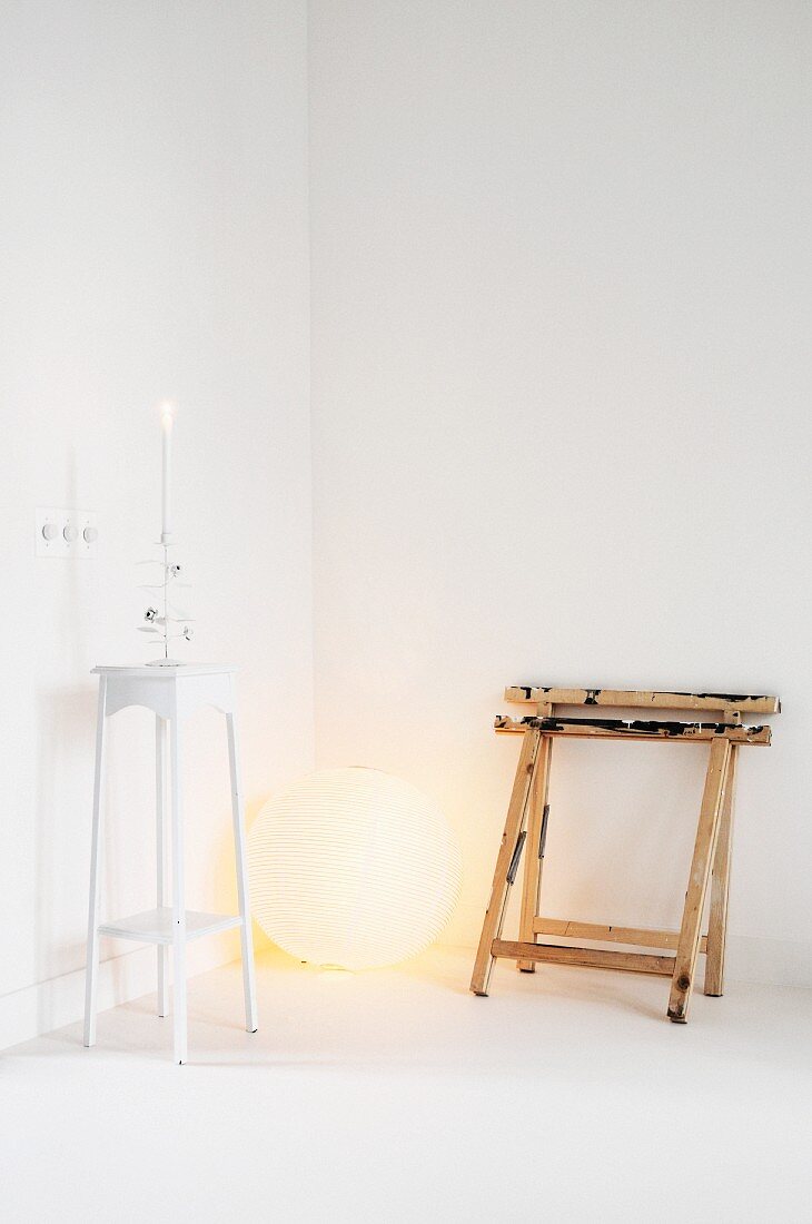 White interior: two painters' trestles leaning against wall next to spherical lamp and plant stand