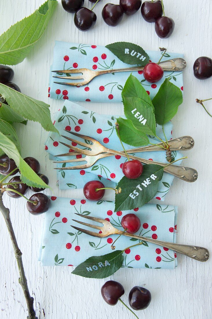 Cherries, napkins, cake forks and names written on cherry leaves