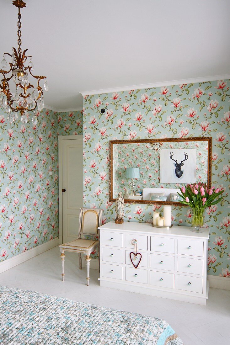 White chest of drawers below framed mirror on floral wallpaper in rustic bedroom