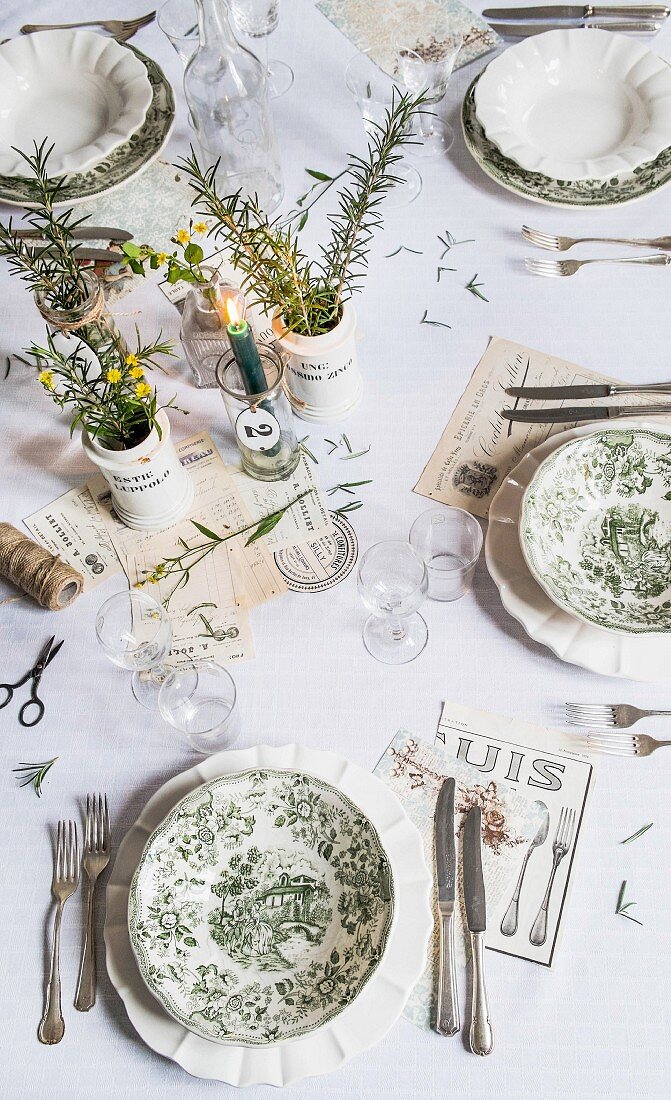 Table set with vintage toile de jouy plates, lit candle and vases of herbs