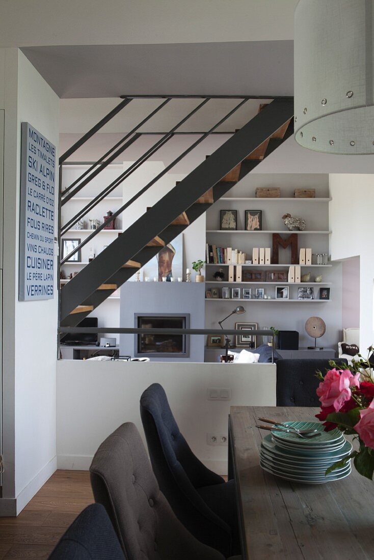 View from dining area into elegant, open-plan interior with steel staircase and wall-mounted shelves