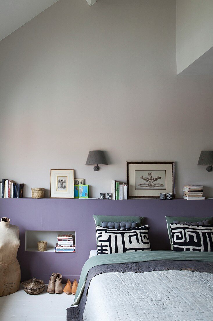 Modernes Schlafzimmer mit mauvefarbenem Bettkopfteil, Bücherstapel, schwarz-weißen Kissenbezügen und Vintage-Schneiderpuppe