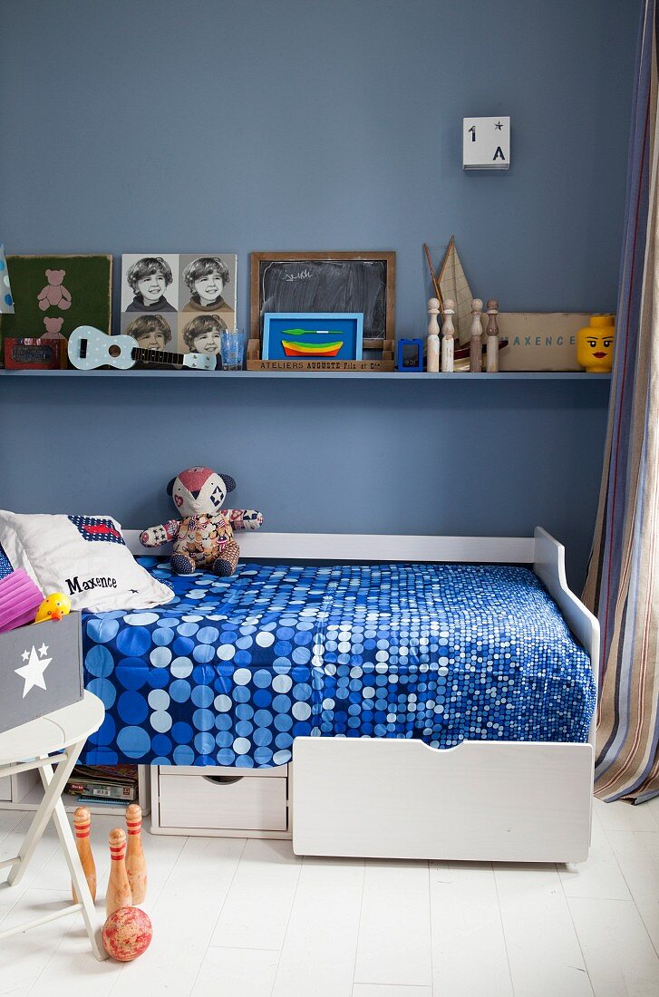 Weißes Bett mit Bettschubladen in Jungenzimmer mit nostalgischem Spielzeug und blauer Wand
