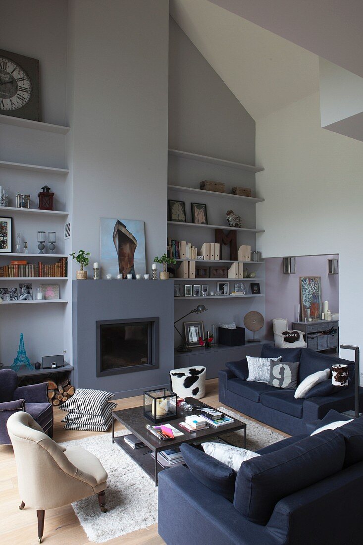 High-ceilinged lounge area with fireplace and floating shelves on pale lilac wall