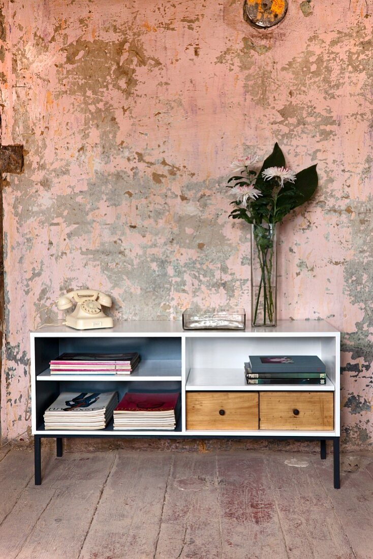 Upcycling - open-fronted sideboard painted white with wooden drawers against wall with peeling paint