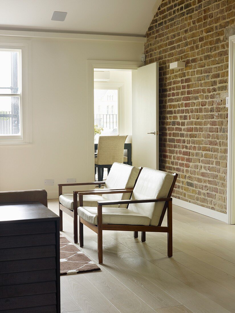 Sessel mit hellen Polstern auf Holzgestell im Wohnzimmer, im Hintergrund Ziegelwand