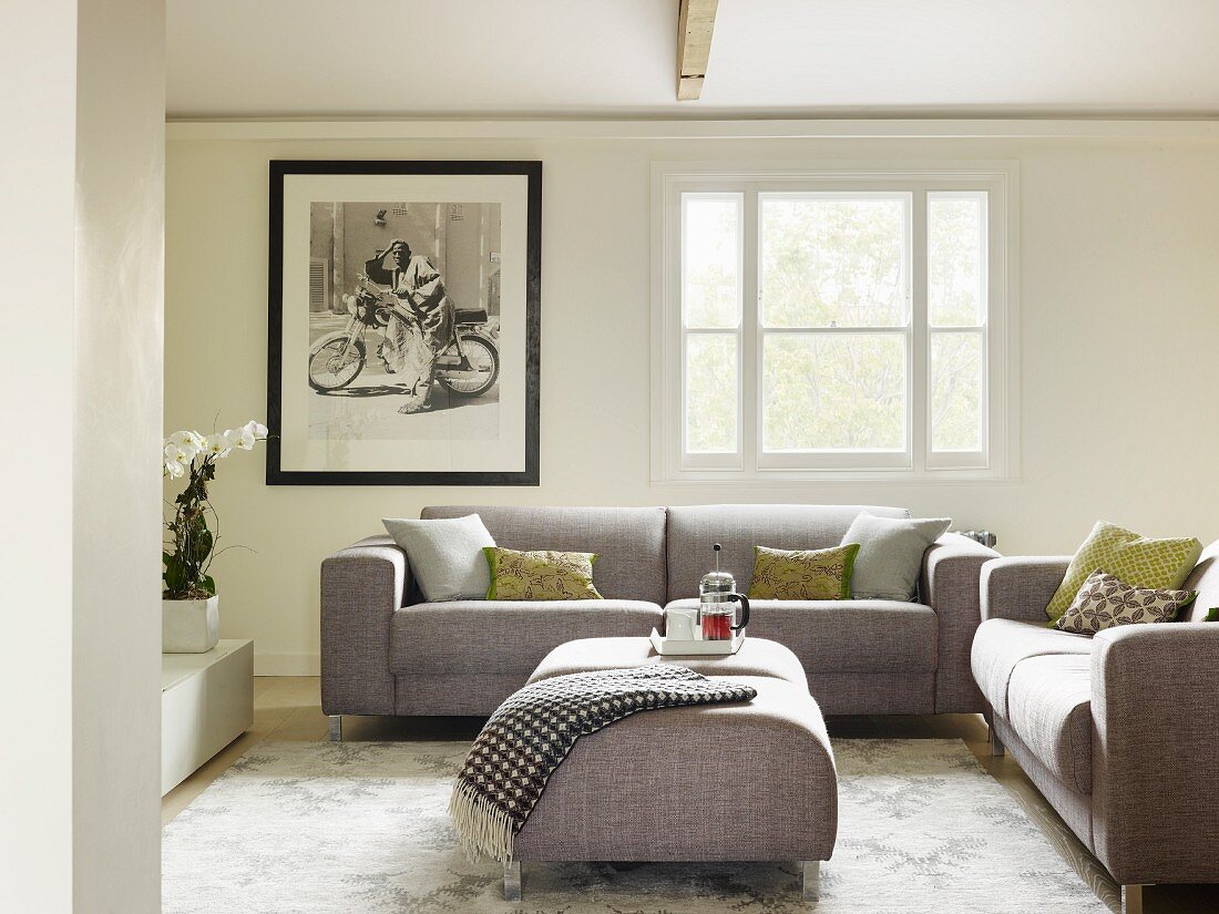 Moderne, graue Polstersofagarnitur mit passendem Hocker als Couchtisch in traditionellem Wohnzimmer, an Wand schwarz-weisses-Foto