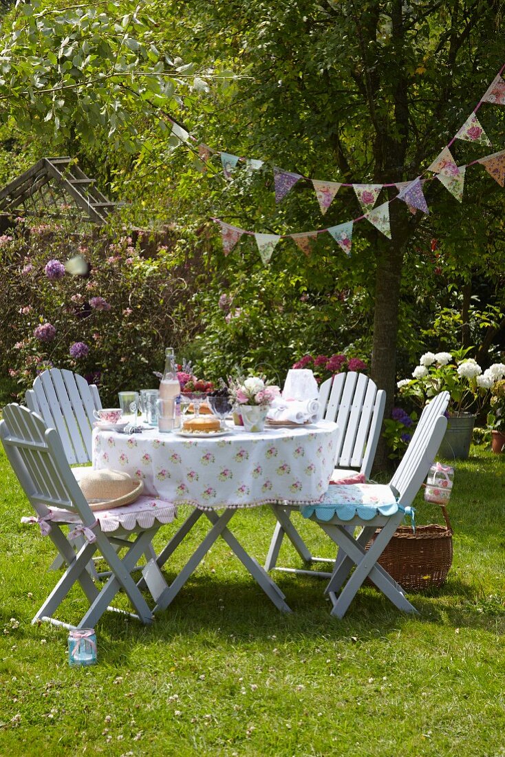 Summer garden party with romantic set table, comfortable garden chairs with seat cushions and vintage-style bunting