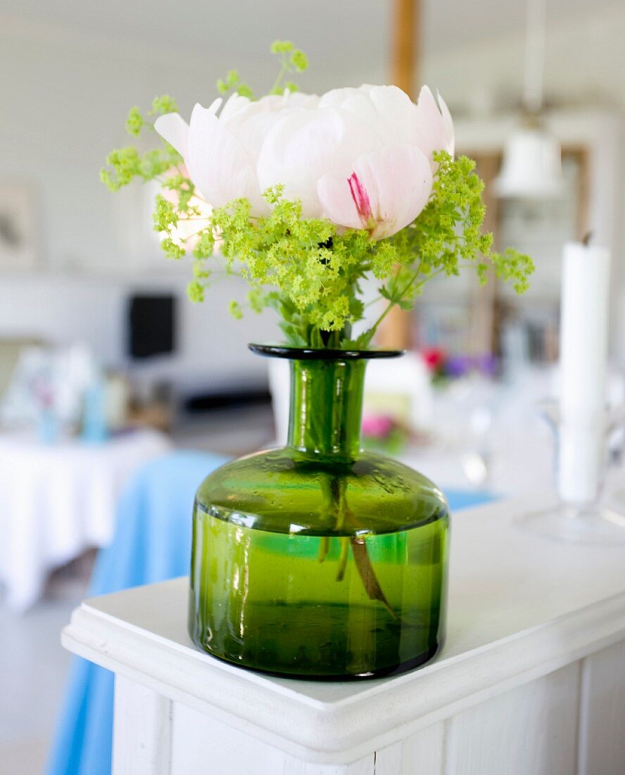 Peony in green vintage bottle on white wooden surface