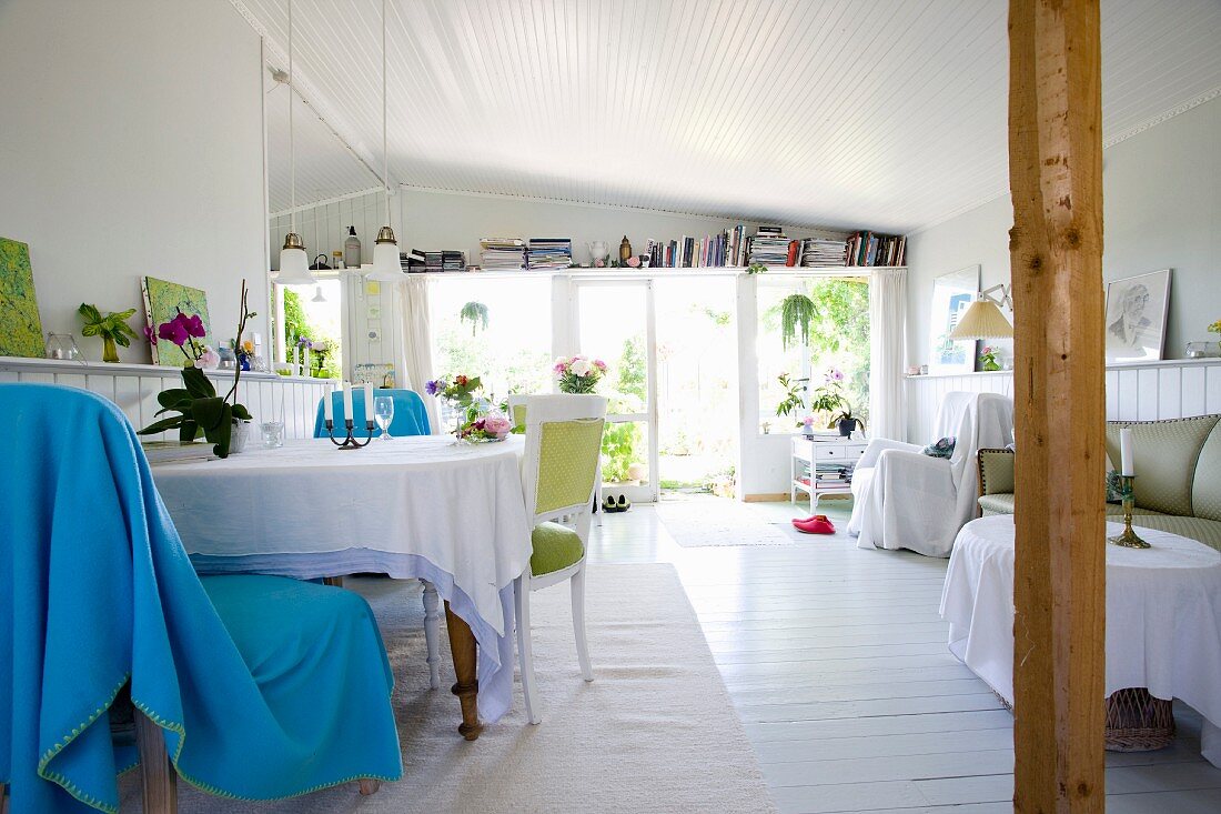 Hellblaue Decke über Stuhl am Tisch mit Tischdecke in offenem Cottage Wohnzimmer mit weißem Dielenboden