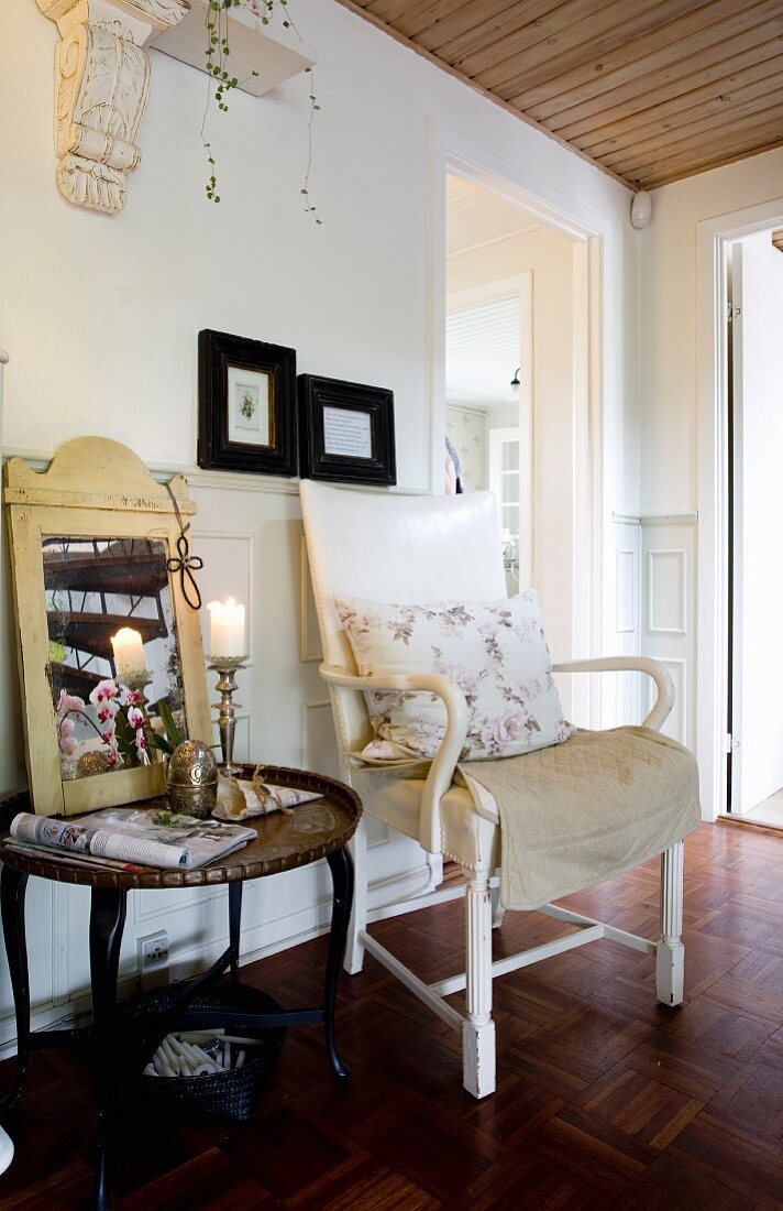 Traditional chair with cushion next to side table decorated with candlestick and mirror against wainscoting in foyer