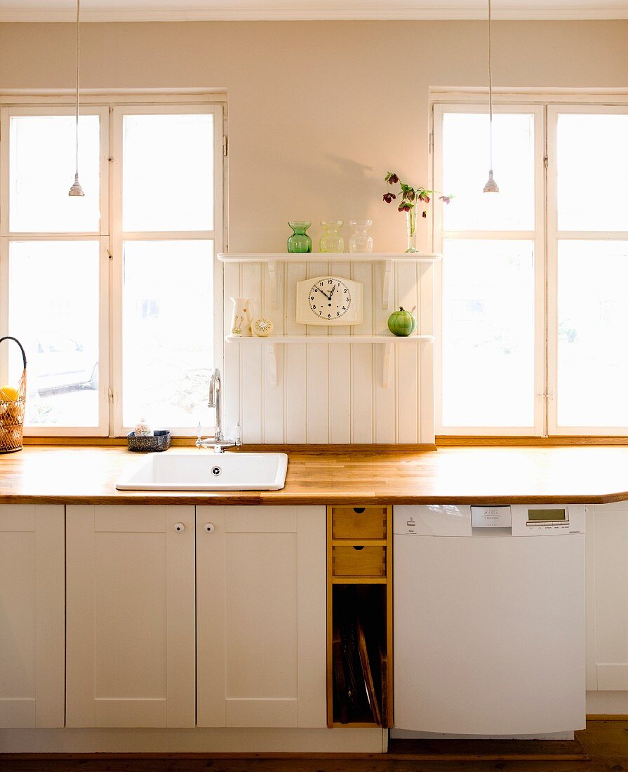 Kitchen counter with wooden worksurface and white cabinets below window in rustic interior