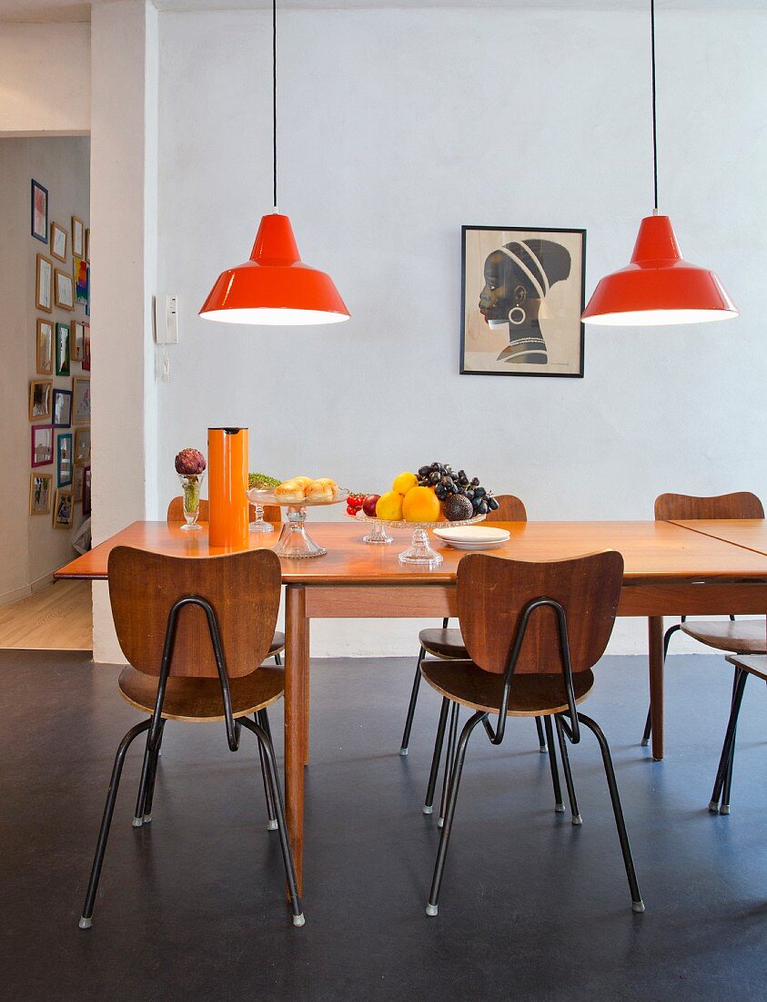 Glass bowls on extendible table with retro school chairs and orange pendant lamps in dining area