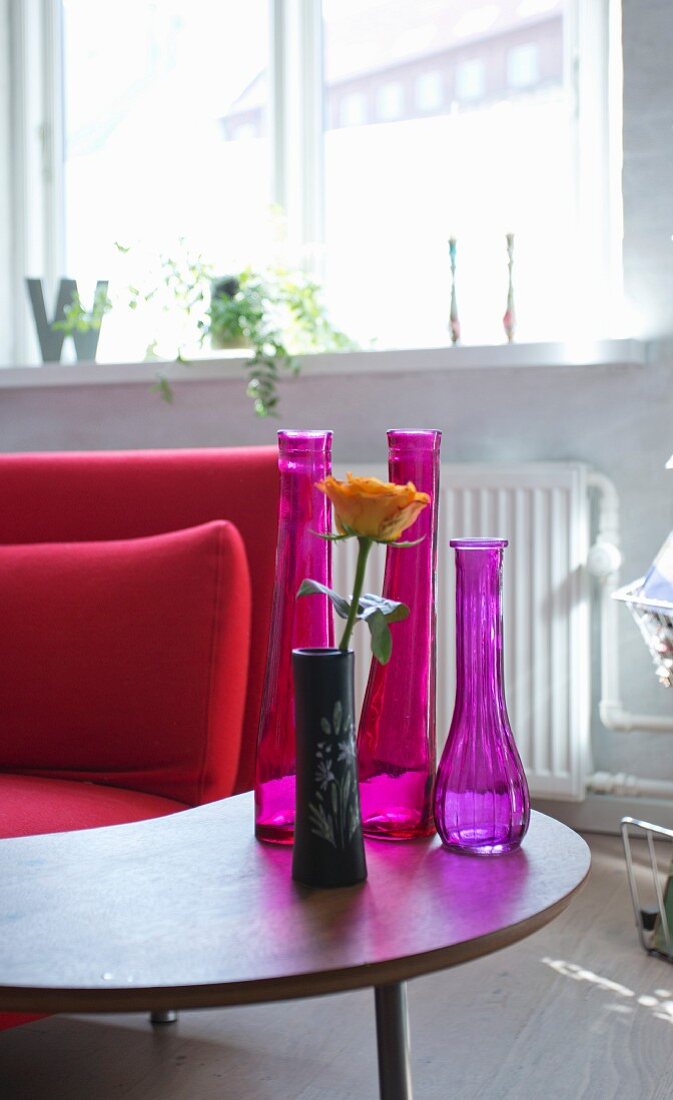 Arrangement verschiedener Vasen auf Retrotischchen neben rotem Sofa im Wohnbereich