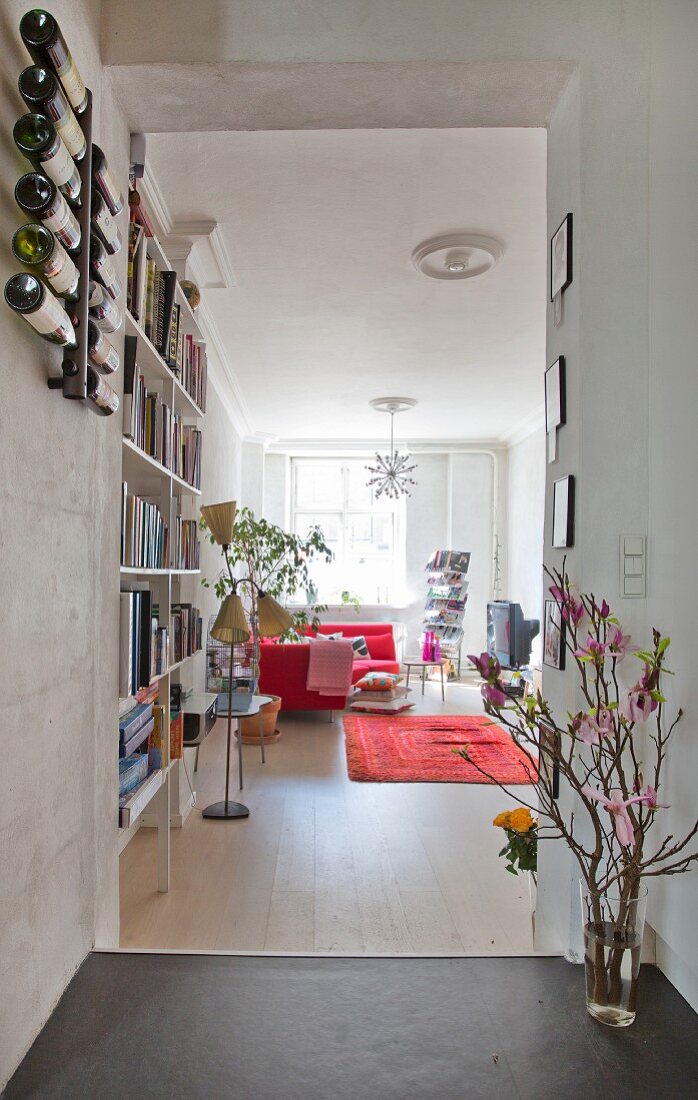 Blick in gemütlichen offenen Wohnbereich mit Bücherregal, Retro Stehlampe und Blütenzweig im Durchgang einer renovierten Stadtwohnung