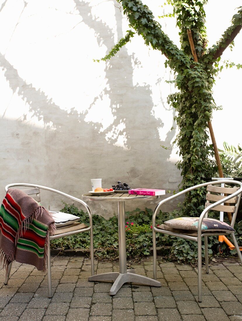 Terrassenplatz mit Bistromöbel auf Pflastersteinboden und Efeu beranktem Baum im Innenhof