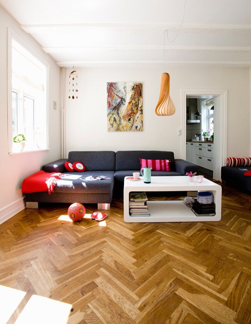 Interior with elegant herringbone parquet floor, modern white coffee table and dark grey sofa combination in corner in renovated period building