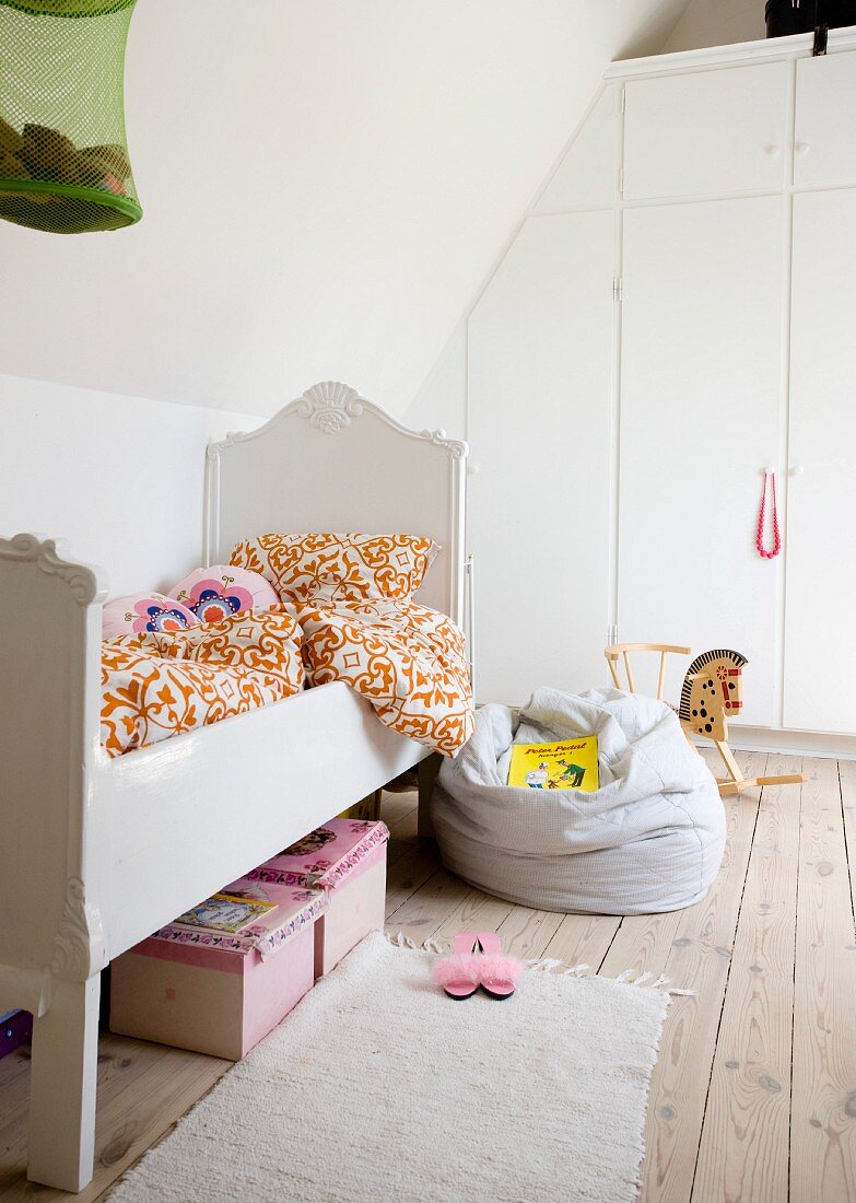 White, child's bed with vintage-style frame and beanbag on wooden floor in front of white fitted wardrobes