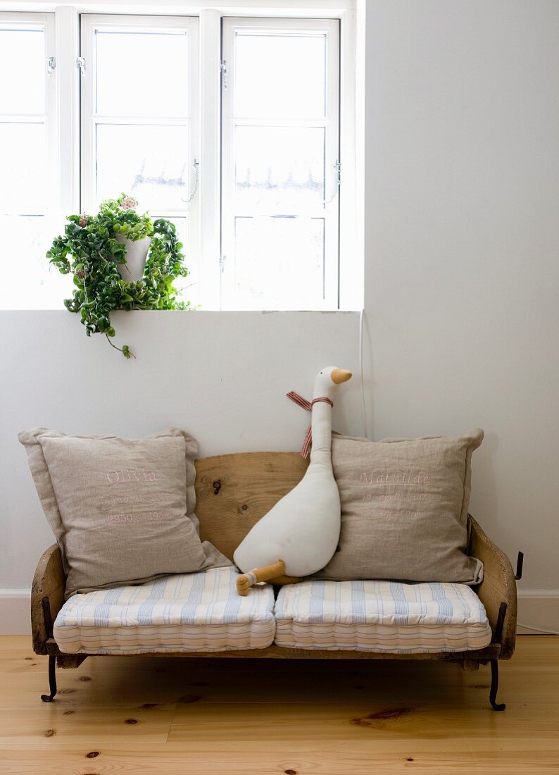 Fabric goose toy sitting on vintage-style children's sofa made from old sledge below window
