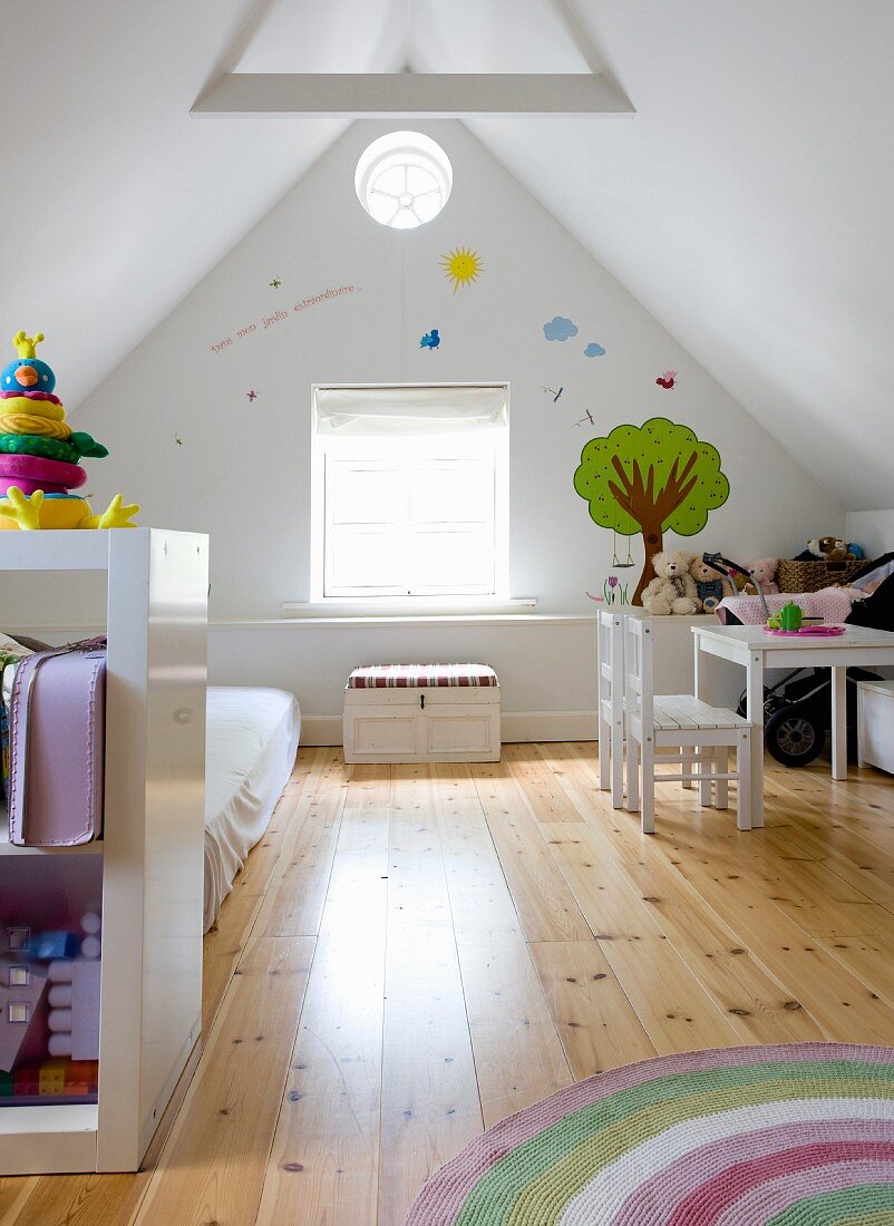 Child's bedroom in converted attic; shelving in front of futon on wooden floor, child's table and chairs against gable-end wall