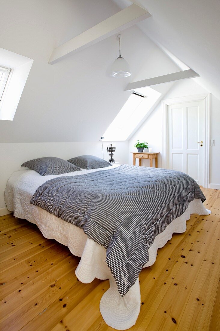 Schwarz-weiss gestreifte Tagesdecke auf Doppelbett in weißem Schlafzimmer in ausgebautem Dach mit Dielenboden