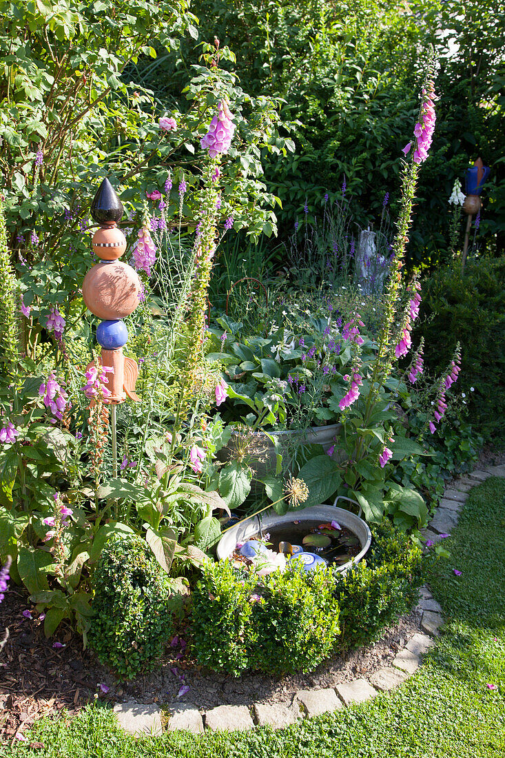 Hellvioletter Fingerhut im Beet mit Randstreifen aus Pflastersteinen, Gartendeko