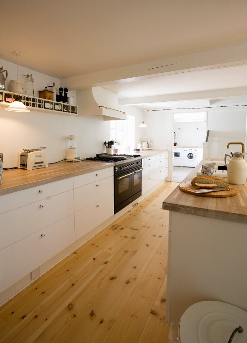 Kitchen counter with white base units in spacious kitchen with wooden floor and open doorway leading into utility room