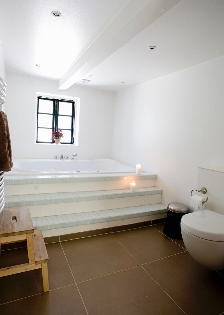 Modernes Bad mit braunen Bodenfliesen, Stufen vor eingebauter Badewanne am Fenster