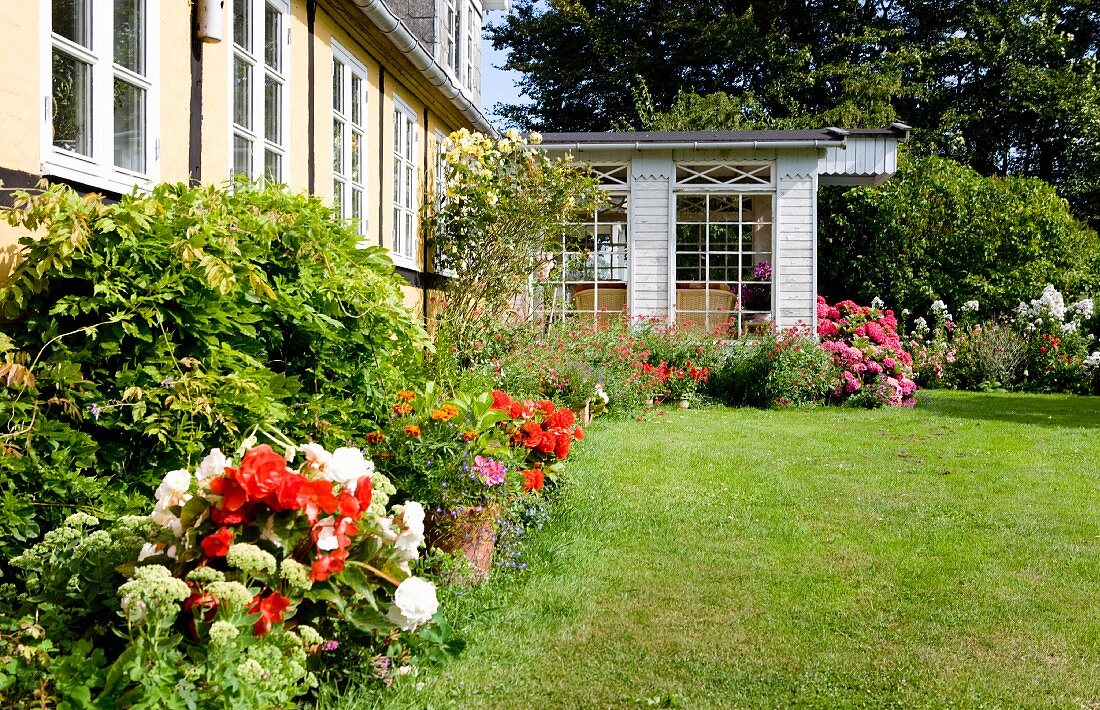 Sommerlicher Garten mit gemähtem Rasen und blühende Blumen vor Wohnhaus mit Anbau