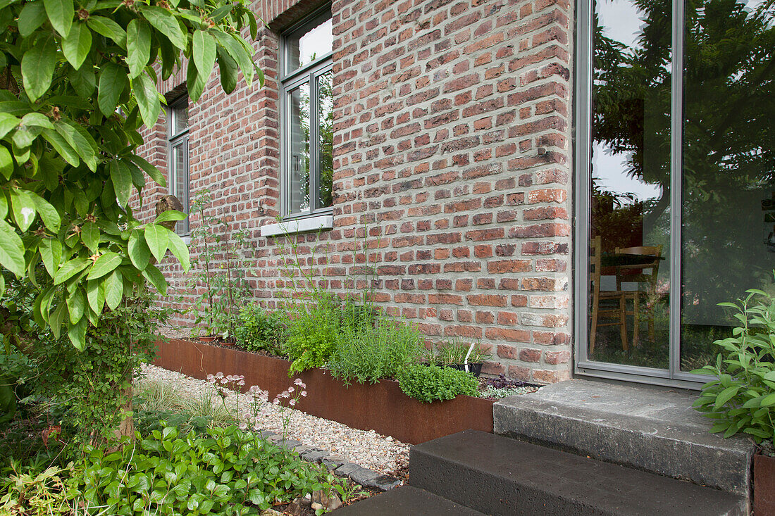 Steps leading to glass door in brick façade next to raised bed with rusty metal surround