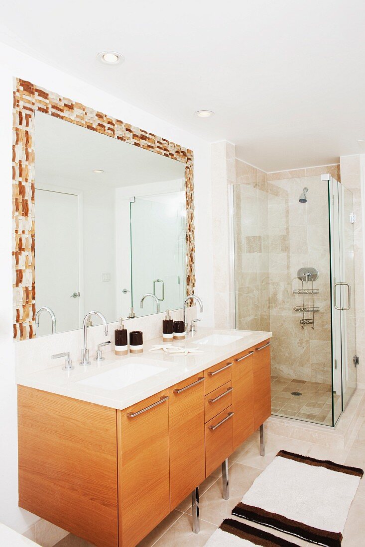 Modern bathroom with washstand, wooden base cabinets, mirror with mosaic frame and glass shower cubicle