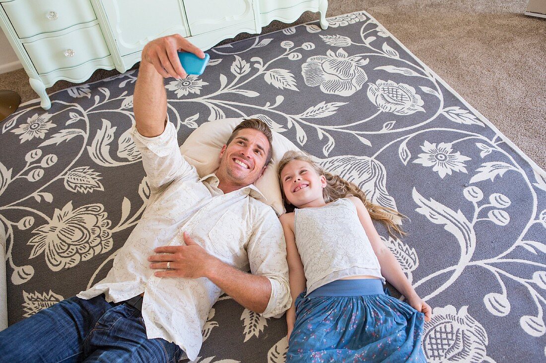 Father and daughter lying on rug taking selfie