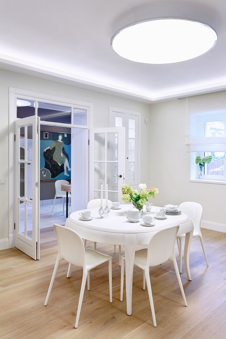 Large, round ceiling lamp above white dining set and view of modern artwork through open double glass doors