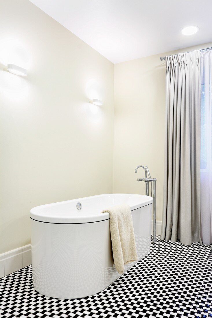 Freistehende Designerwanne und Bodenarmatur in elegantem Bad mit bodenlangen Vorhängen und schwarz-weißem Mosaikboden
