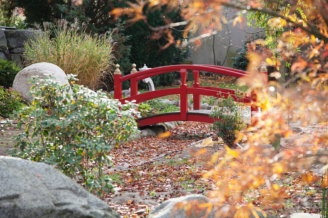 Red-painted wooden bridge spanning gravel bed in Japanese-style garden