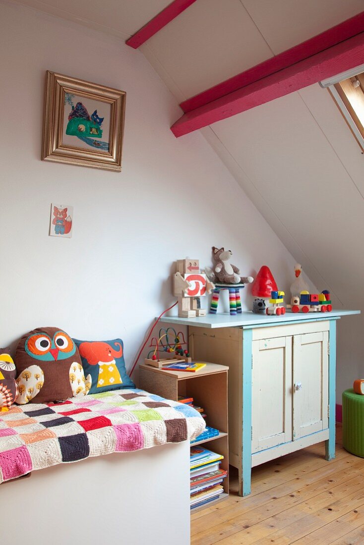 Ablage mit Patchworkdecke, im Hintergrund ländliche Kommode mit Spielsachen in Kinderzimmer unter dem Dach