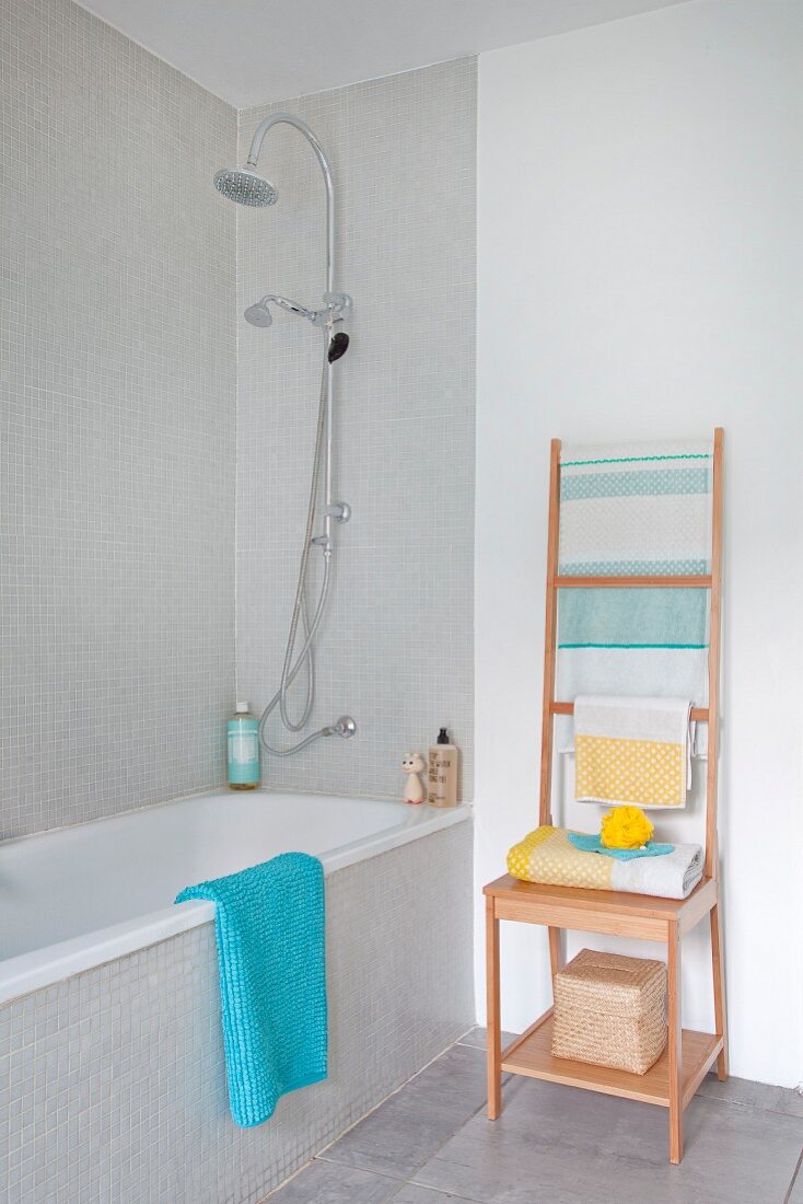 Holzhocker mit leiterartiger Lehne für Handtücher, neben Badewanne im Badezimmer