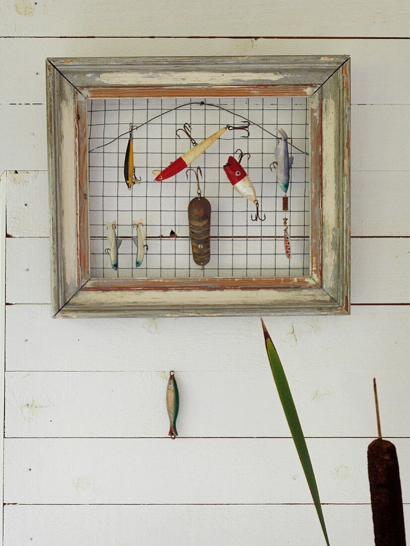 Various anglers' lures hung from wire mesh in vintage picture frame