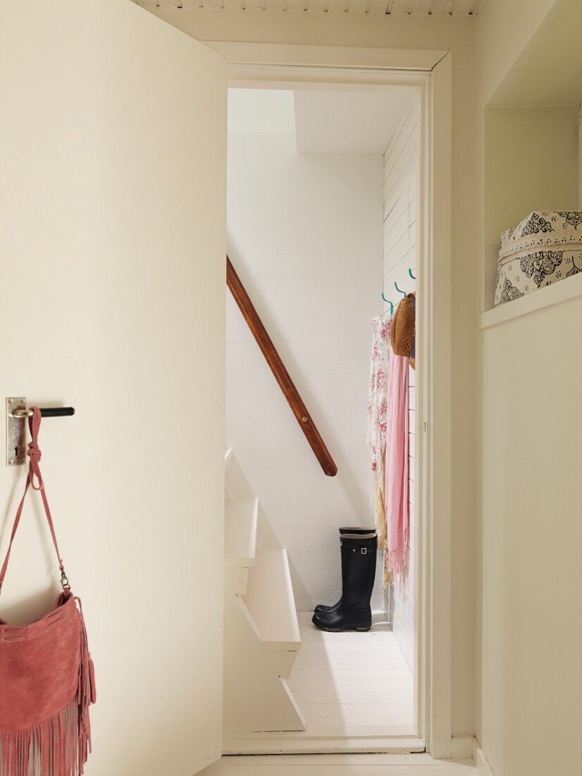 Blick durch geöffnete Tür auf weiß lackierte Holzstiege mit Handlauf, schwarze Gummistiefel und Tücher an Wandhaken